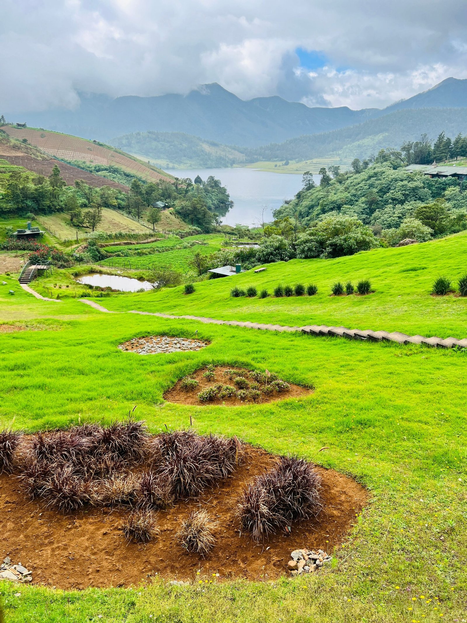 Beautiful green landscape with hills, trees, and a tranquil lake set against a mountainous backdrop.