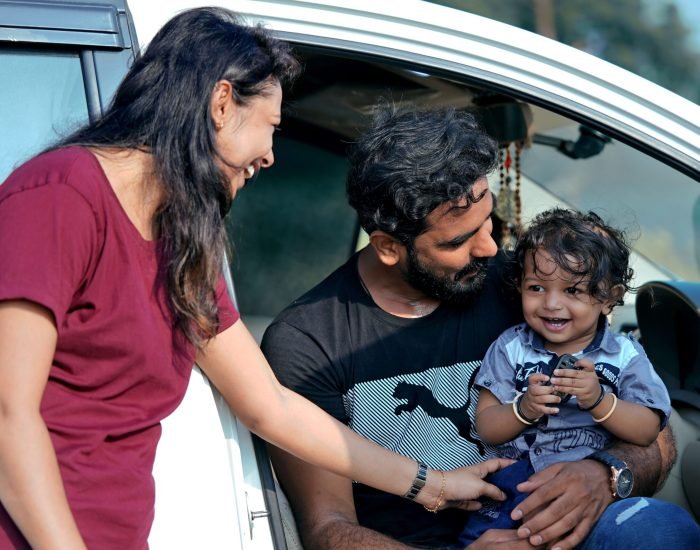A joyful family moment with parents and child sitting in a car in Sanand, India.