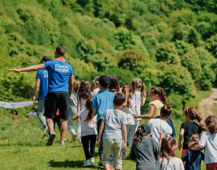 A group of children with coaches walking outdoors in a lush green area during a school trip.